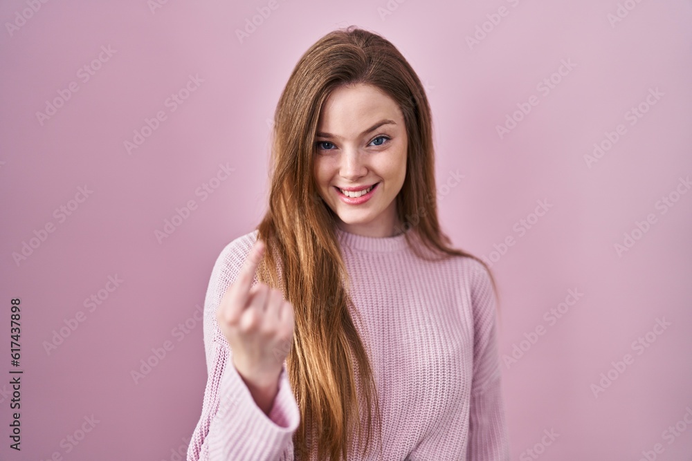 Young caucasian woman standing over pink background beckoning come here gesture with hand inviting welcoming happy and smiling Young caucasian woman standing over pink background beckoning come here gesture with hand inviting welcoming happy and smiling