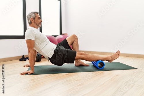 Middle age grey-haired man using foam roller stretching at sport center photo