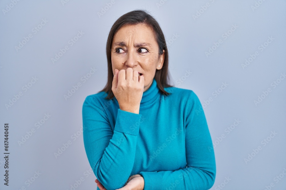 Middle age hispanic woman standing over isolated background looking stressed and nervous with hands on mouth biting nails. anxiety problem. Middle age hispanic woman standing over isolated background looking stressed and nervous with hands on mouth biting nails. anxiety problem.