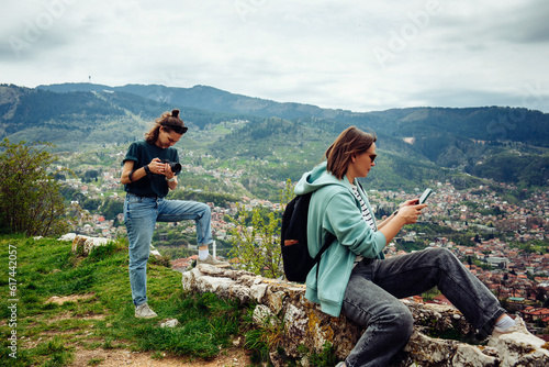 One female friend takes pictures of another during a photo shoot in a big European city in mountains. The work of photo and video stockers in travel
