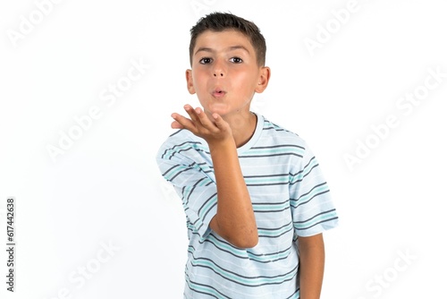 Little hispanic boy wearing striped T-shirt looking at the camera blowing a kiss with hand on air being lovely and sexy. Love expression.