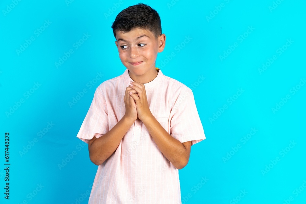 Little hispanic boy wearing white shirt steepled fingers and looks mysterious aside has great evil plan in mind Little hispanic boy wearing white shirt steepled fingers and looks mysterious aside has great evil plan in mind