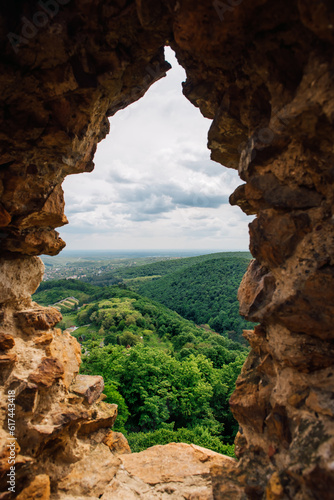 Picturesque view of the valley and green hills covered with dense green forest through the window of ancient stone buildings. Ancient fortifications