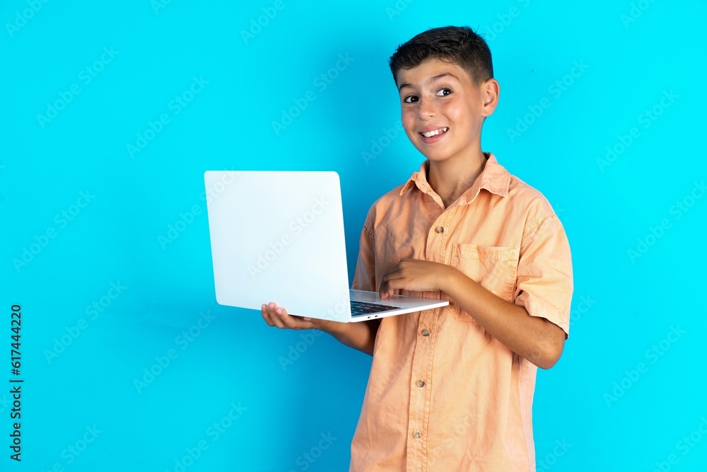 Adorable Little hispanic boy wearing orange shirt holding modern device Adorable Little hispanic boy wearing orange shirt holding modern device