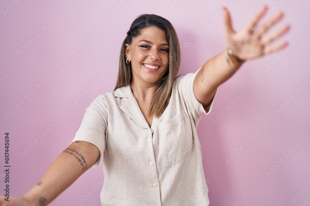 Blonde woman standing over pink background looking at the camera smiling with open arms for hug. cheerful expression embracing happiness. Blonde woman standing over pink background looking at the camera smiling with open arms for hug. cheerful expression embracing happiness.