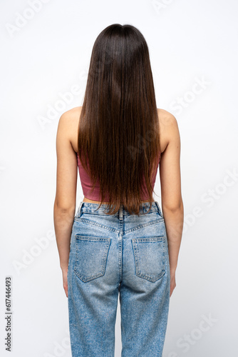 Back view of beautiful brunette with long hair standing isolated on gray background