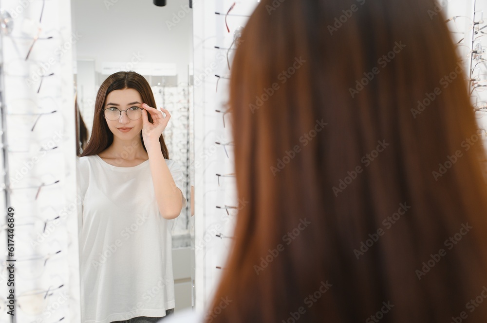 eyesight and vision concept - young woman choosing glasses at optics store.