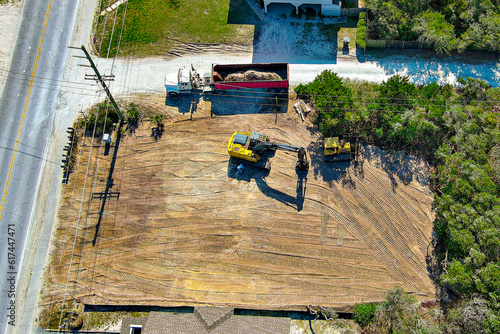 Aerial perspective of a yellow excavator preparing a vacant lot. 