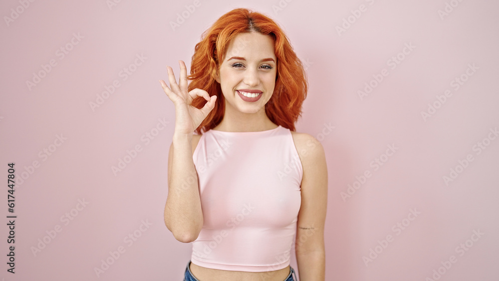 Young redhead woman smiling with ok gesture over isolated pink background Young redhead woman smiling with ok gesture over isolated pink background