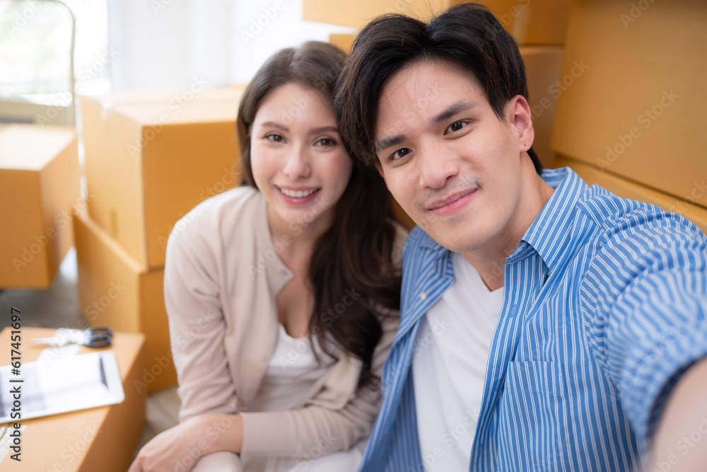 ํYoung asian couple take a selfie with cardboard boxes in new home ํYoung asian couple take a selfie with cardboard boxes in new home
