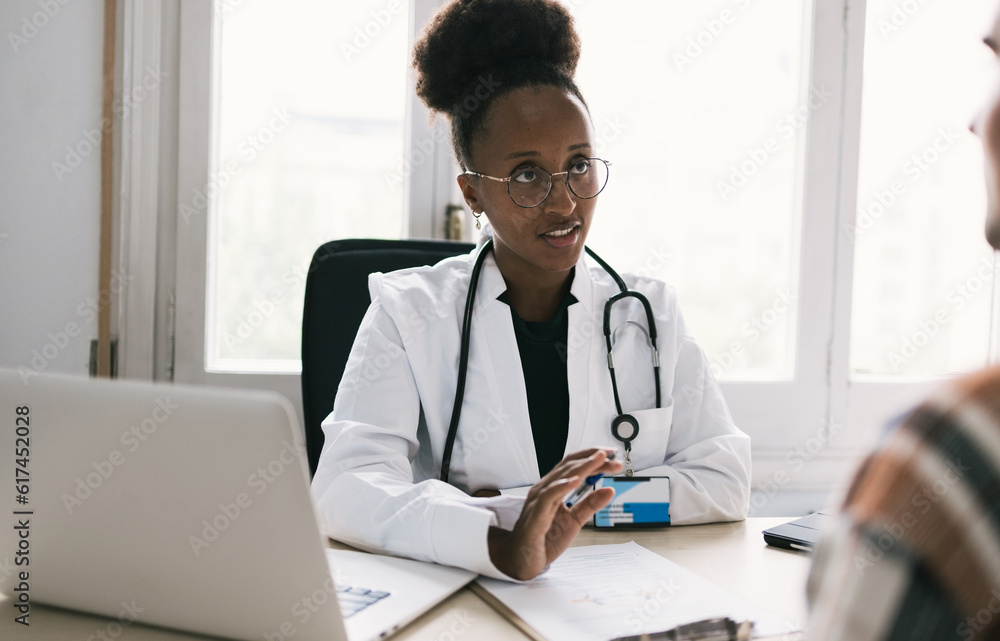 Serious black woman doctor sitting at table with patient Serious black woman doctor sitting at table with patient