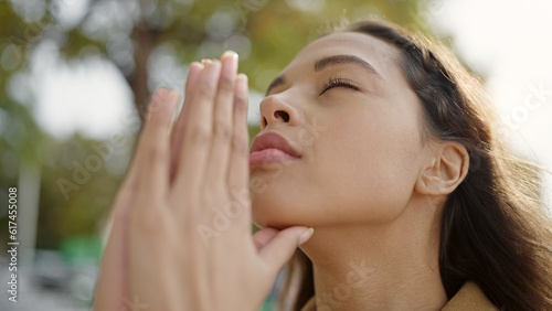Young beautiful hispanic woman praying with closed eyes at park