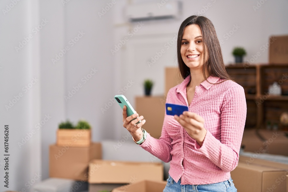 Young beautiful hispanic woman using smartphone and credit card at new home Young beautiful hispanic woman using smartphone and credit card at new home