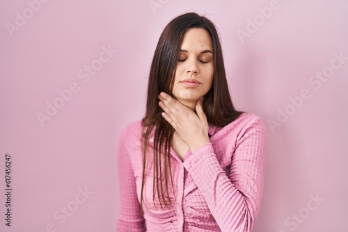 Young hispanic woman standing over pink background touching painful neck, sore throat for flu, clod and infection