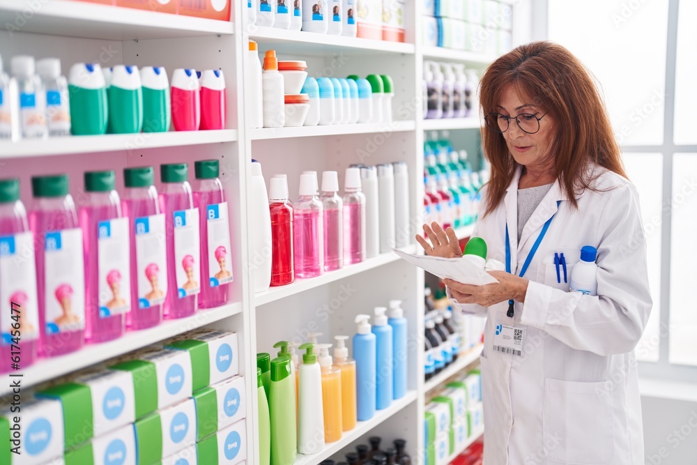 Middle age woman pharmacist holding bottle reading prescription at pharmacy