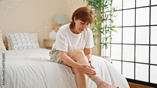 Photos Middle age woman applying lotion on leg sitting on bed at bedroom