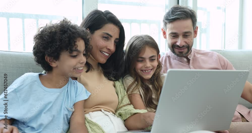 Beautiful married multiethnic couple and little 8s son and daughter resting on couch, discuss purchase, watch family movie, enjoy e-shopping spend carefree leisure together at home using modern laptop Beautiful married multiethnic couple and little 8s son and daughter resting on couch, discuss purchase, watch family movie, enjoy e-shopping spend carefree leisure together at home using modern laptop