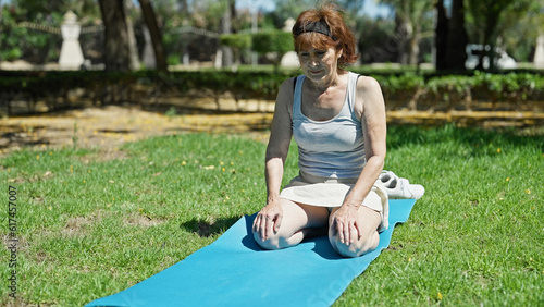 Middle age woman sitting on knees on yoga mat with serious face at park