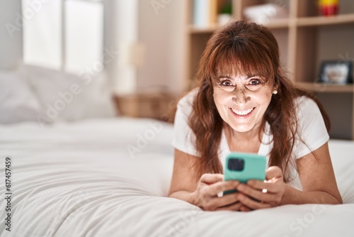 Middle age woman using smartphone lying on bed at bedroom