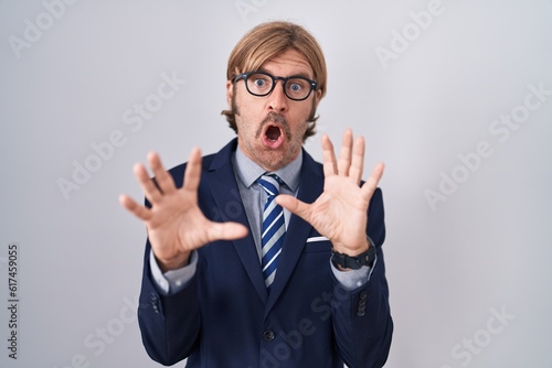 Caucasian man with mustache wearing business clothes afraid and terrified with fear expression stop gesture with hands, shouting in shock. panic concept.