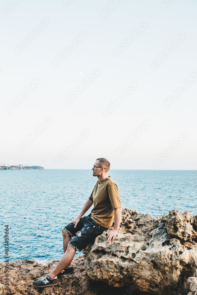 A young guy is sitting on the seashore and enjoying the sunset A young guy is sitting on the seashore and enjoying the sunset