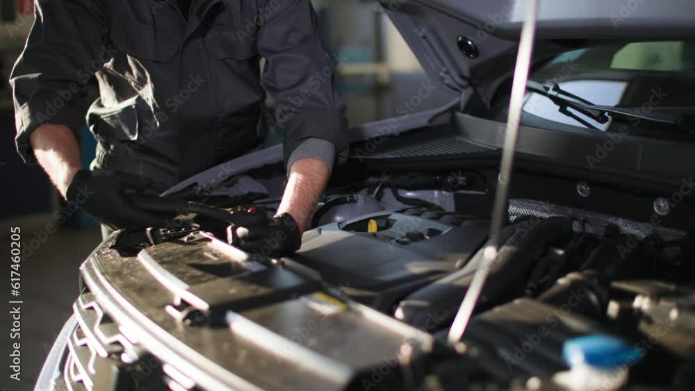 auto maintenance, young man in uniform repairs car engine with wrench backdrop of sun rays, close-up auto maintenance, young man in uniform repairs car engine with wrench backdrop of sun rays, close-up
