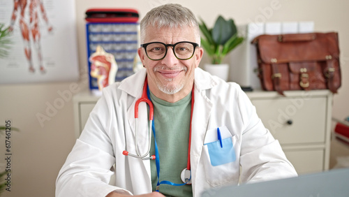 Middle age grey-haired man doctor using laptop working at clinic