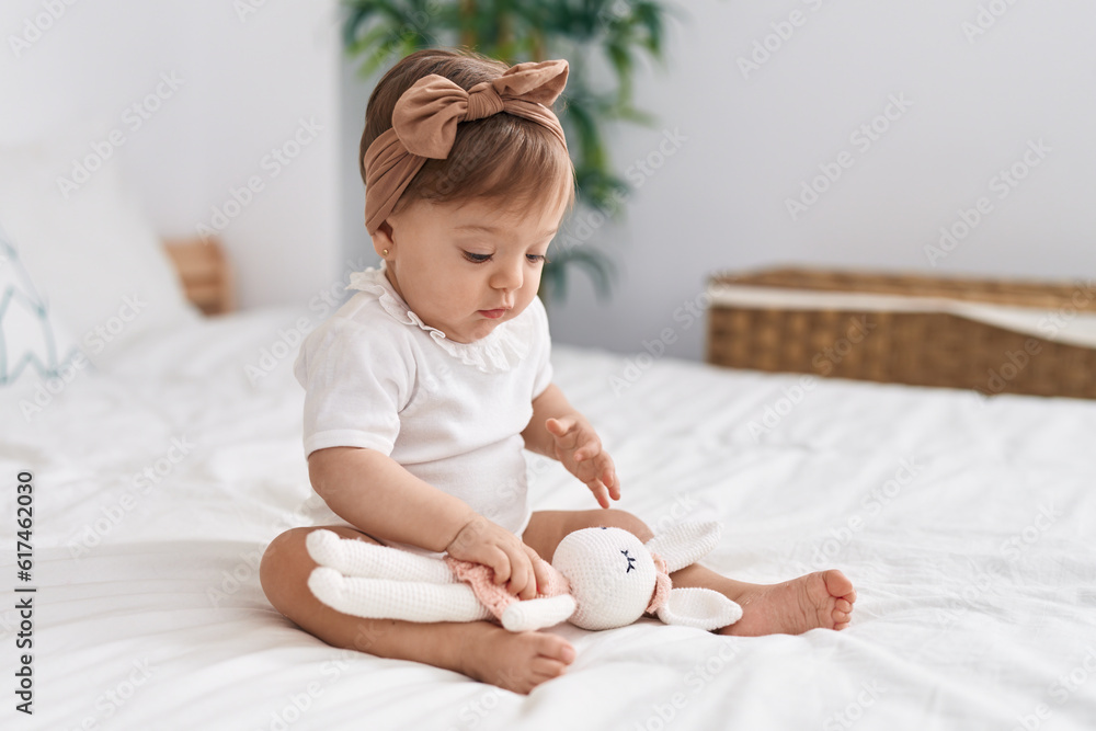 Adorable caucasian baby sitting on bed playing with doll at bedroom Adorable caucasian baby sitting on bed playing with doll at bedroom
