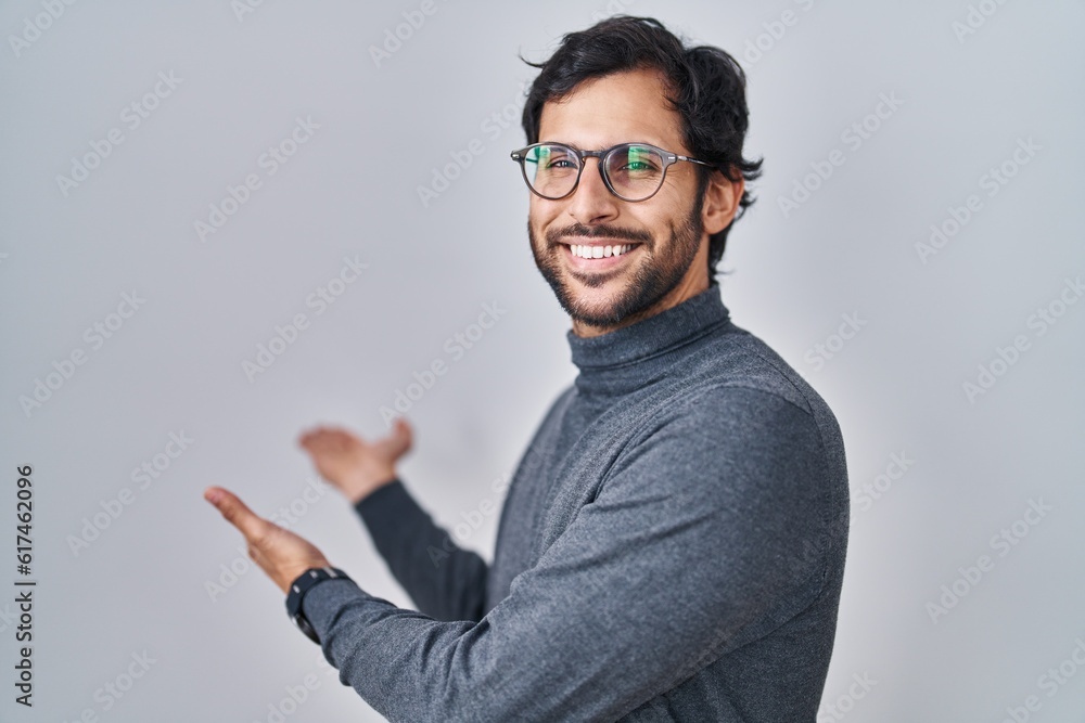 Handsome latin man standing over isolated background inviting to enter smiling natural with open hand Handsome latin man standing over isolated background inviting to enter smiling natural with open hand