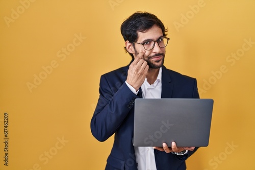Handsome latin man working using computer laptop pointing to the eye watching you gesture, suspicious expression