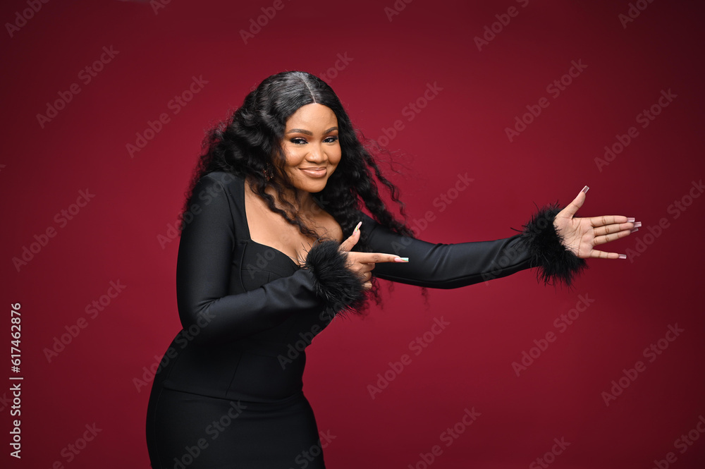 Photo of a happy young and beautiful woman standing isolated over red wall background. She is looking at the camera and showing Copy space pointing. Product placement Photo of a happy young and beautiful woman standing isolated over red wall background. She is looking at the camera and showing Copy space pointing. Product placement