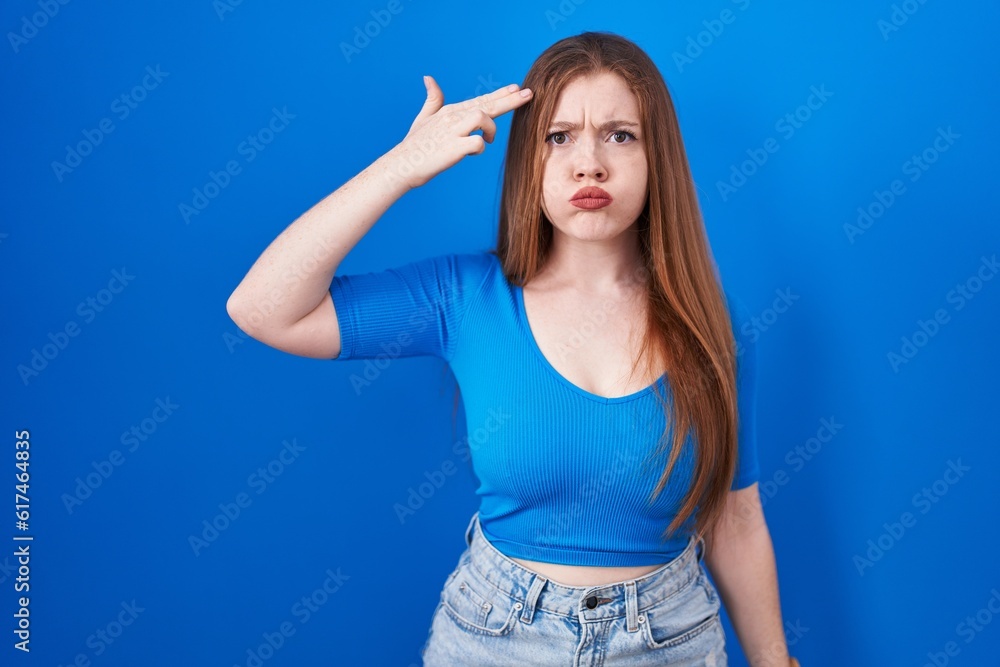 Redhead woman standing over blue background shooting and killing oneself pointing hand and fingers to head like gun, suicide gesture. Redhead woman standing over blue background shooting and killing oneself pointing hand and fingers to head like gun, suicide gesture.
