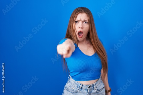 Redhead woman standing over blue background pointing displeased and frustrated to the camera, angry and furious with you