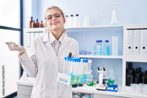 Young caucasian woman working at scientist laboratory holding samples screaming proud, celebrating victory and success very excited with raised arm