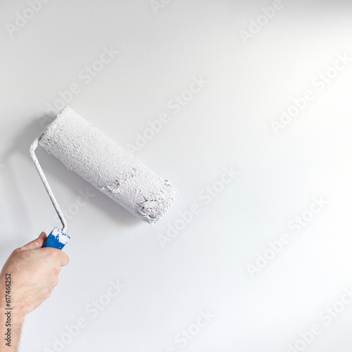 Painting apartment, renovating with white color paint. Male hand painting wall with paint roller.