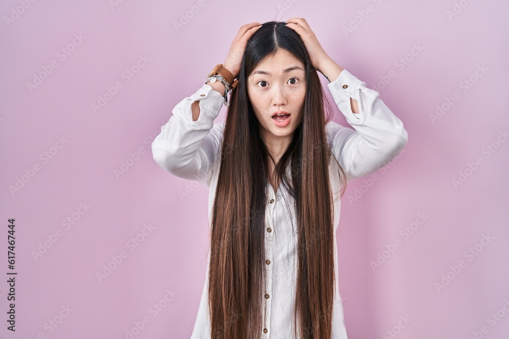 Chinese young woman standing over pink background crazy and scared with hands on head, afraid and surprised of shock with open mouth Chinese young woman standing over pink background crazy and scared with hands on head, afraid and surprised of shock with open mouth