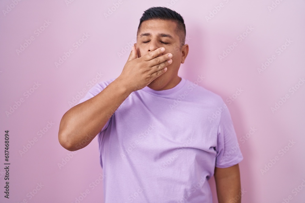 Young hispanic man standing over pink background bored yawning tired covering mouth with hand. restless and sleepiness. Young hispanic man standing over pink background bored yawning tired covering mouth with hand. restless and sleepiness.