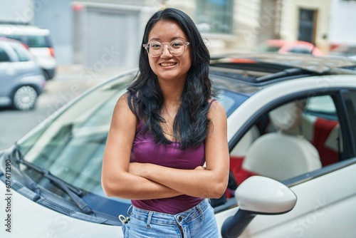 Young chinese woman smiling confident leaning on car with arms crossed gesture at street