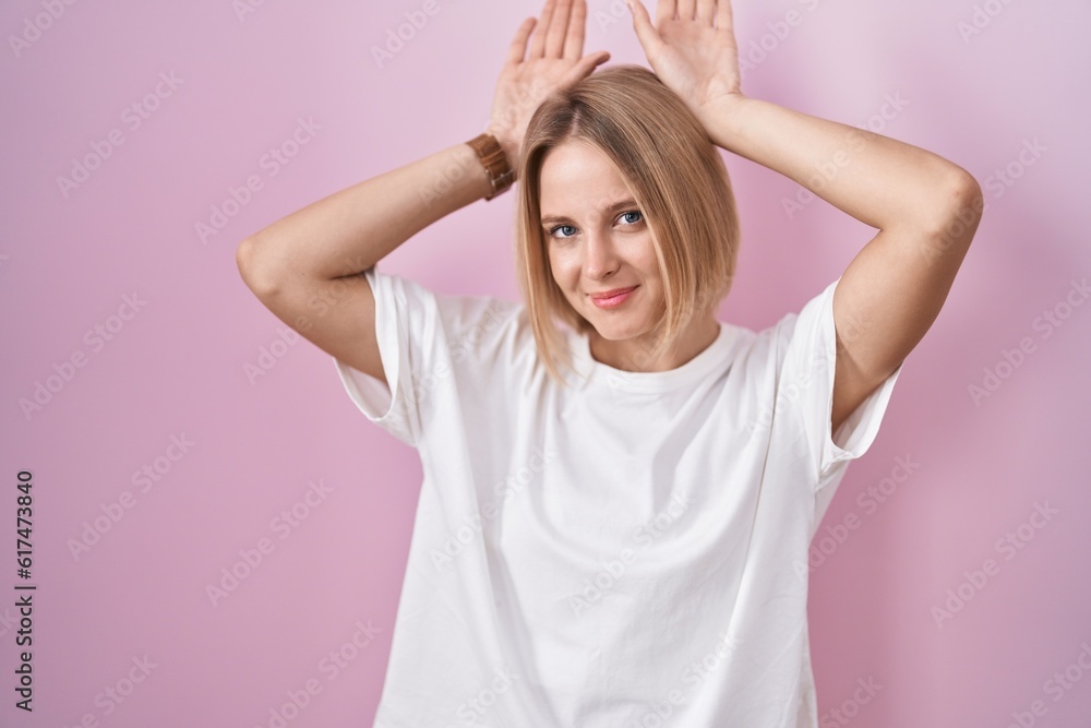 Young caucasian woman standing over pink background doing bunny ears gesture with hands palms looking cynical and skeptical. easter rabbit concept. Young caucasian woman standing over pink background doing bunny ears gesture with hands palms looking cynical and skeptical. easter rabbit concept.