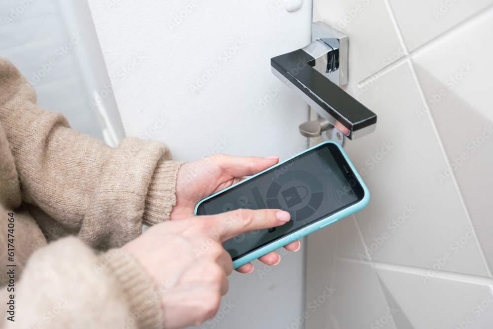 Close-up of woman controlling the security of her house with mobile app on smartphone, she locking the door online Close-up of woman controlling the security of her house with mobile app on smartphone, she locking the door online