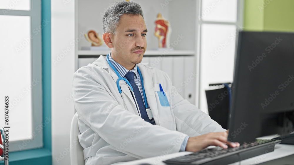 Young hispanic man doctor using computer working at clinic