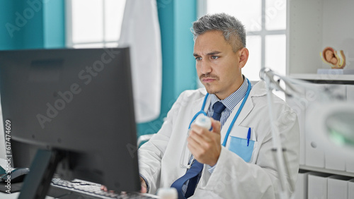 Young hispanic man doctor using computer holding pills at clinic