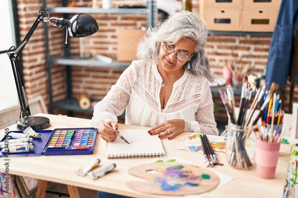 Fototapeta premium Middle age woman artist drawing on notebook at art studio
