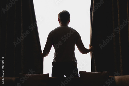 Asian man closing the curtain while watching the view out of the window.