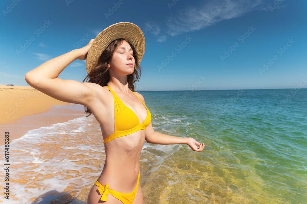 Happiness summer vacation carefree joyful woman standing on sand enjoying tropical beach. Festive girl in bikini relaxing while holding straw hat on caribbean holiday in sea water