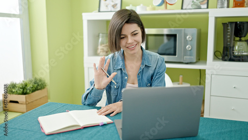 Young caucasian woman having video call sitting on table at home
