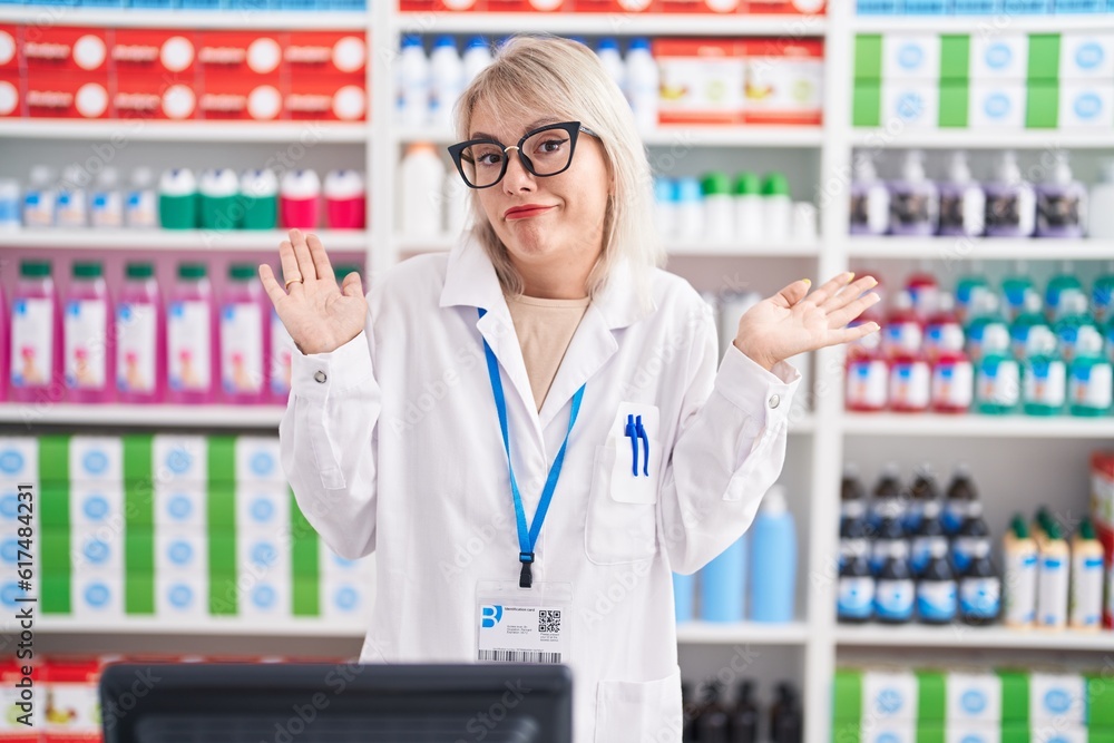 Young caucasian woman working at pharmacy drugstore clueless and confused expression with arms and hands raised. doubt concept. Young caucasian woman working at pharmacy drugstore clueless and confused expression with arms and hands raised. doubt concept.