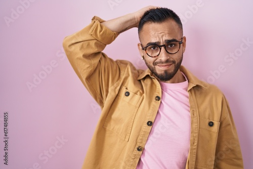 Young hispanic man standing over pink background confuse and wonder about question. uncertain with doubt  thinking with hand on head. pensive concept.