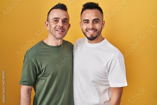 Homosexual couple standing over yellow background with a happy and cool smile on face. lucky person.