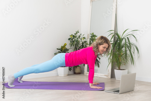 Attractive middle-aged brunette takes a break from exercises while sitting on a gym Mat, and overcame instructional videos online